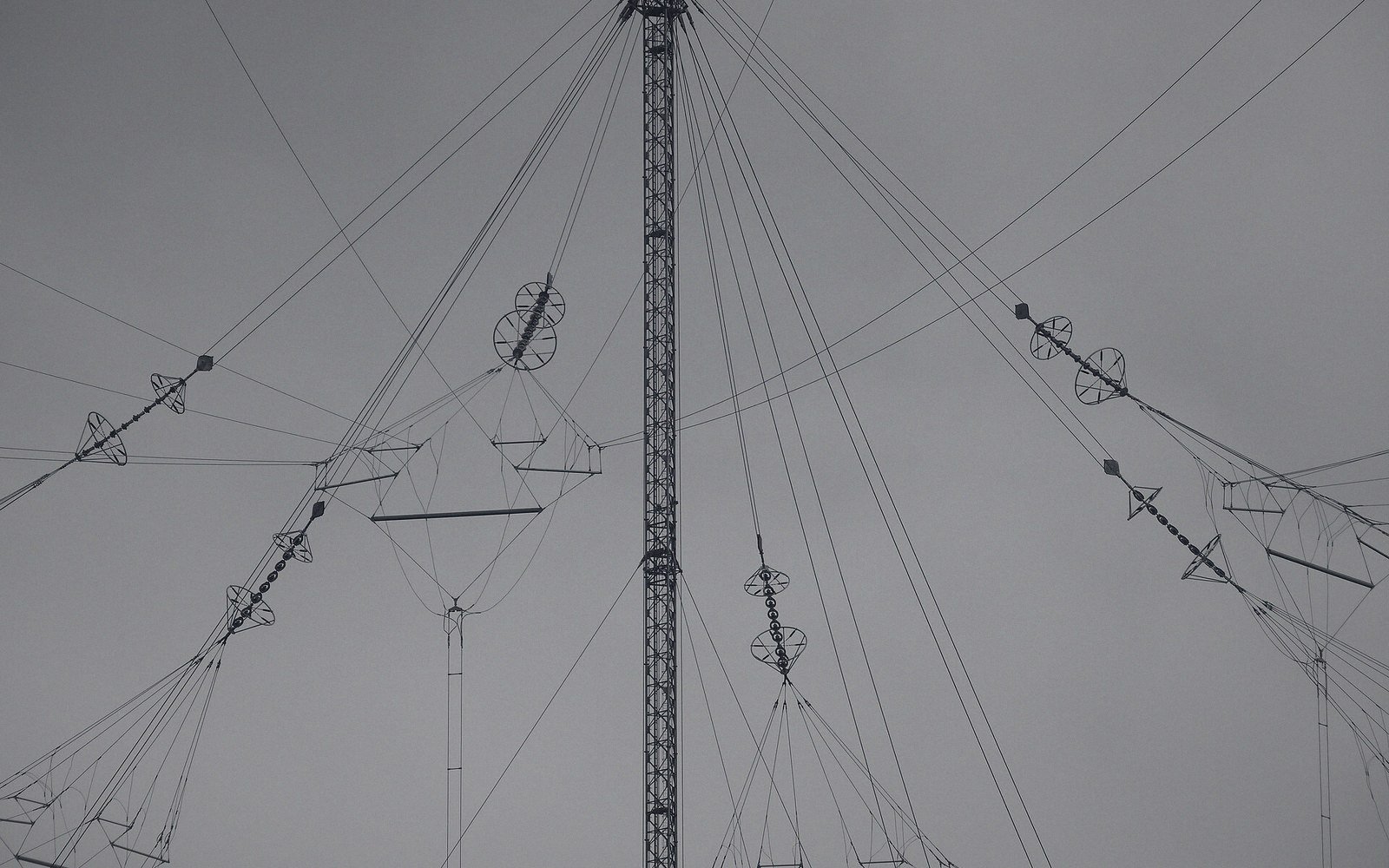 A guyed mast against flat sky with its base insulator visible